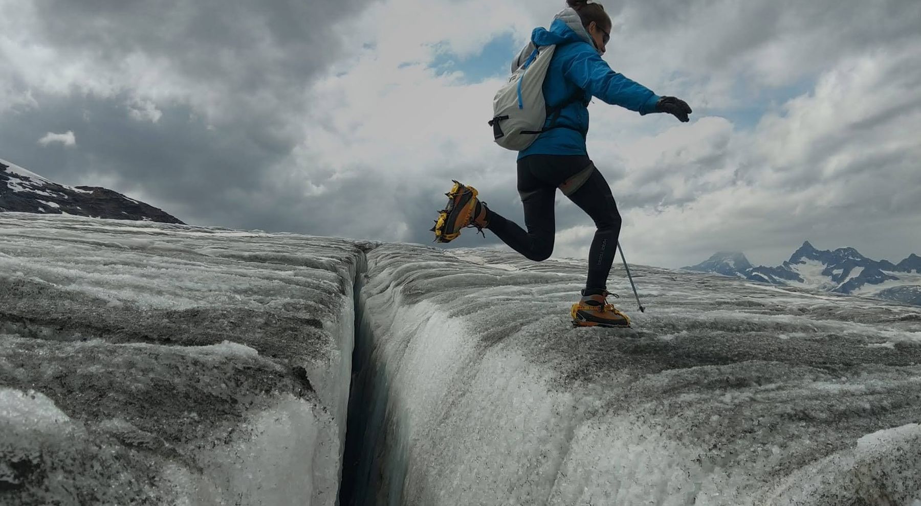 Nathalie franchit d'un saut une crevasse sur un glacier, crampons aux pieds