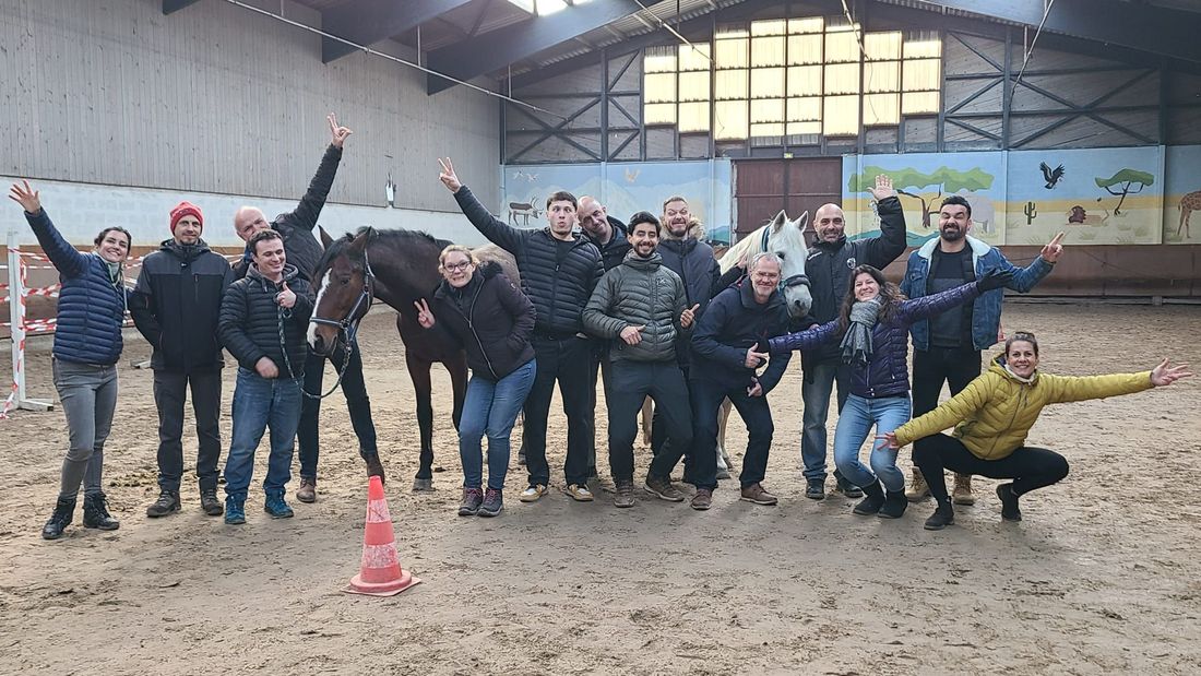Une équipe pose joyeusement avec deux chevaux dans un manège