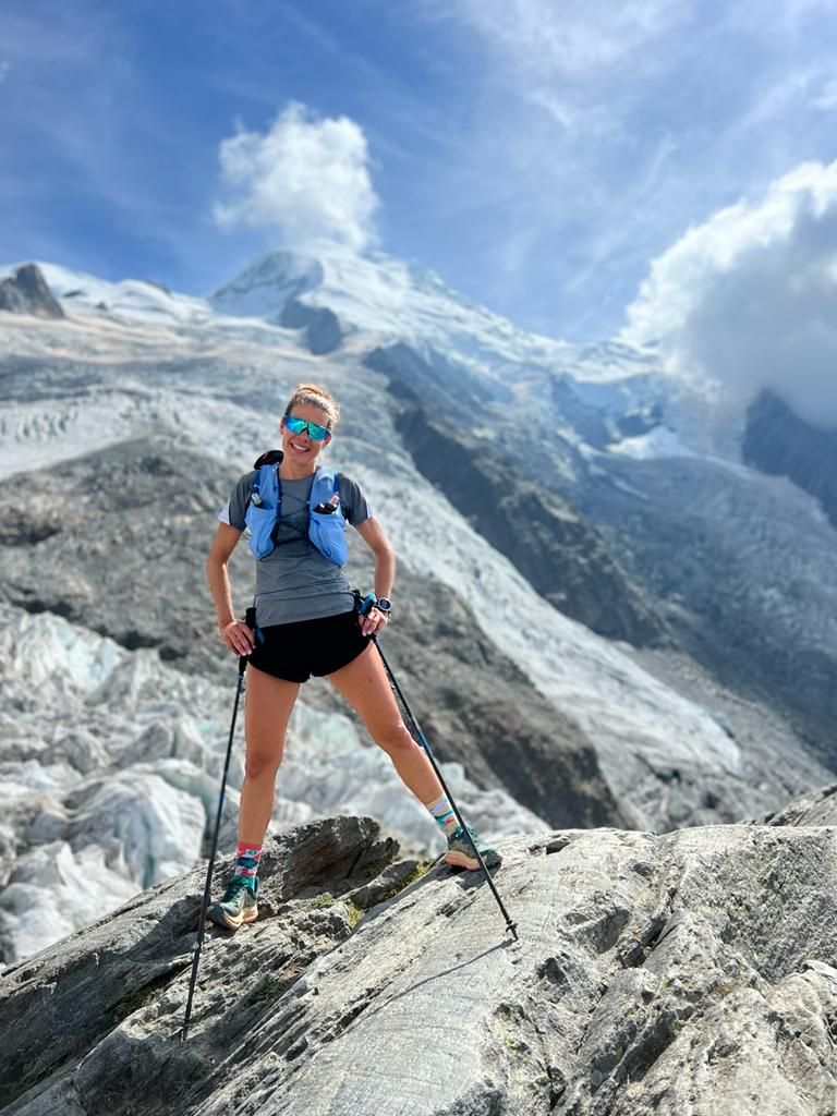 Nathalie debout sur un rocher, bâtons de marche en main, devant le glacier du Mont-Blanc